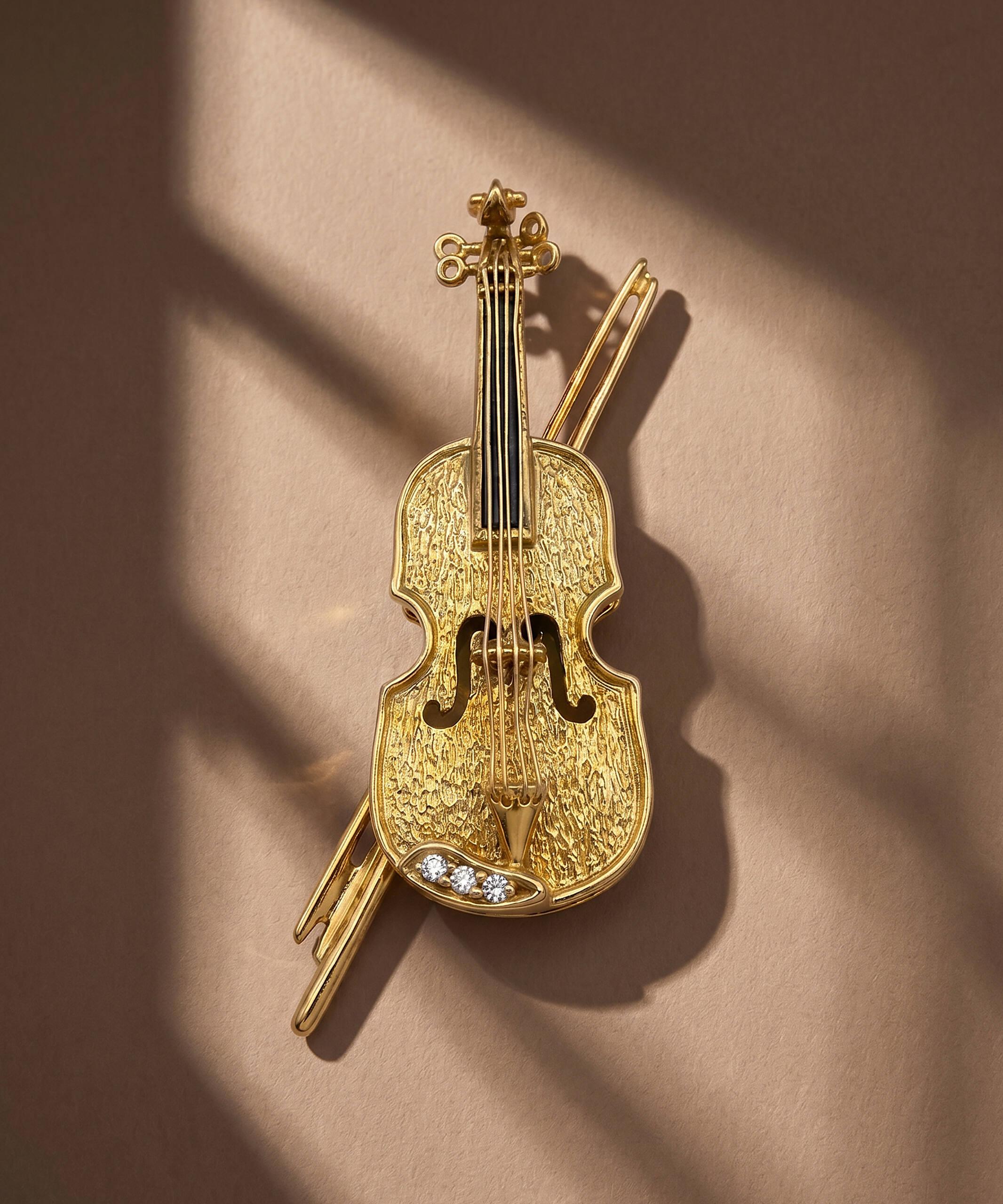 Violin brooch pendant in 18ct Yellow Gold with Diamond accents, shown on a warm neutral background.