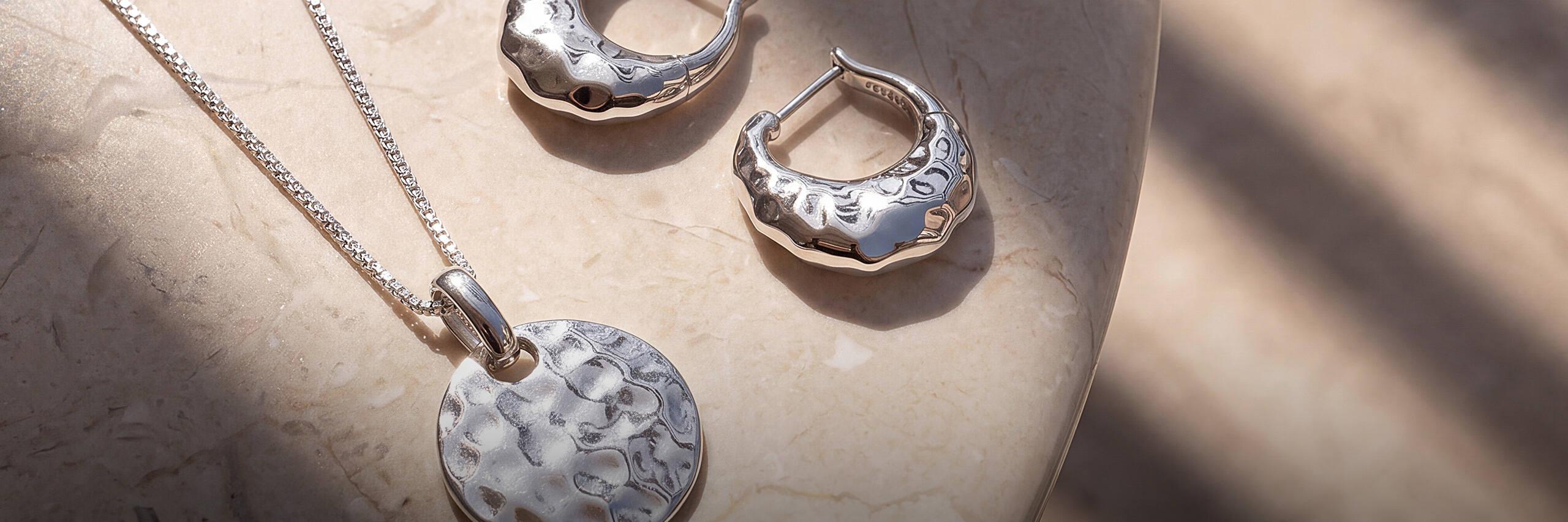 Modern pendant necklace and hoop earrings on a stone surface