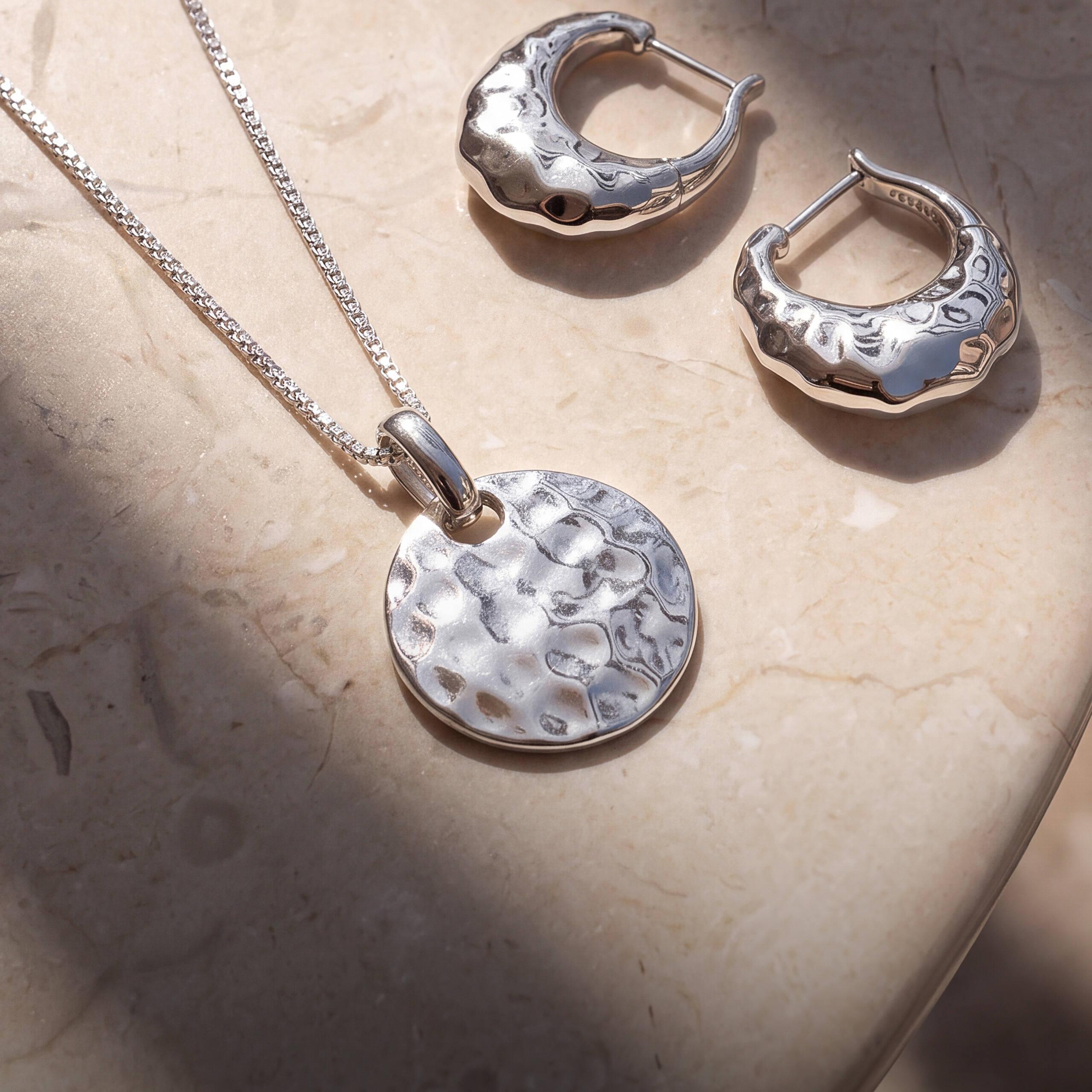 Modern pendant necklace and hoop earrings on a stone surface